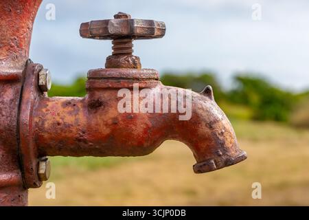 Close up, abstract image of an old, rustic, red well spigot with rust stains on a sunny summer morning. Stock Photo