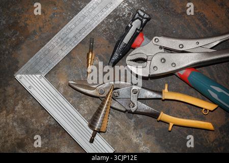 Hammer, metal shears, step drill bits, square and clamp on rusty metal workbench Stock Photo