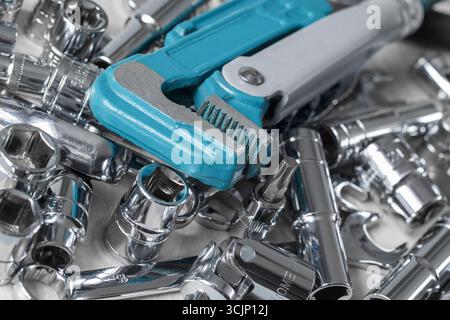 A blue and silver wrench is sitting on top of a pile of various tools. The pile is scattered across a table, with some tools lying on their sides and Stock Photo