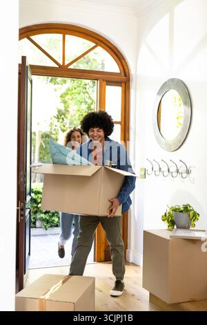 Young diverse couple carrying boxes into new home, smiling and excited for fresh start Stock Photo