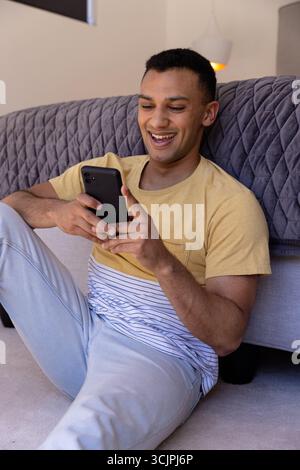 Smiling young man using smartphone while relaxing on floor at home Stock Photo