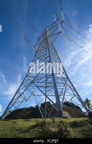 High-voltage pylon from low angle view - A low-angle shot of a high-voltage electricity pylon against a vibrant blue sky with wispy clouds, representi Stock Photo