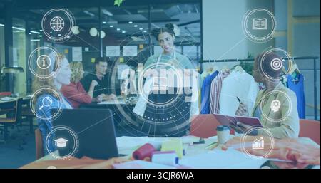 Lead designer wearing gray blazer presenting two garments in open-plan studio, with clothing rack Stock Photo