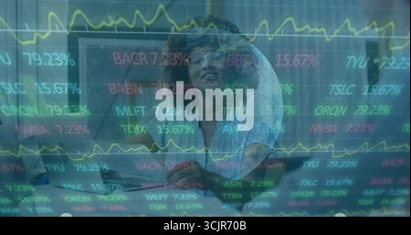 Analyzing female analyst wearing clear glasses monitoring stock tickers on laptop in tech office Stock Photo
