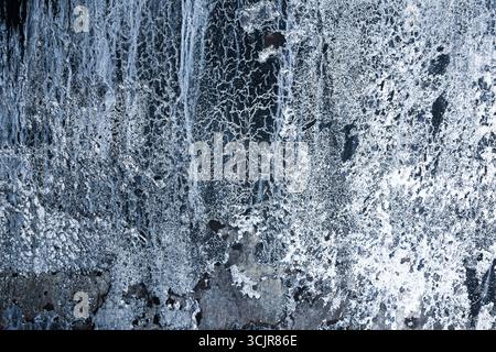 Vertical black rock with ice and snow. Abstraction of an icy rock with snow. Stock Photo