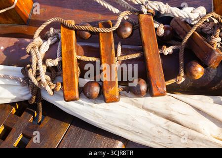 Old ropes with folded sail and a rope ladder on the wooden deck of an old ship, close up Stock Photo