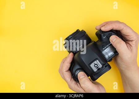 Digital camera in hands of photographer. Hands using digital camera on a yellow background with copy space for text. Top view, minimalism. Stock Photo