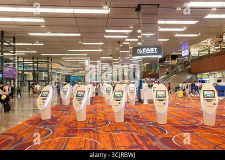 Modern changi singapore airport terminal with rows of automated self-check-in kiosks and travellers walking amidst bright interior lighting Stock Photo