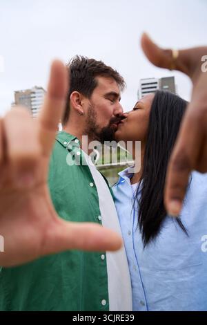 Happy multiracial couple taking a photo framing with hands in a city park Stock Photo