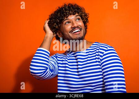 Young man in striped sailor shirt posing against vibrant orange backdrop showcasing cheerful and trendy style Stock Photo