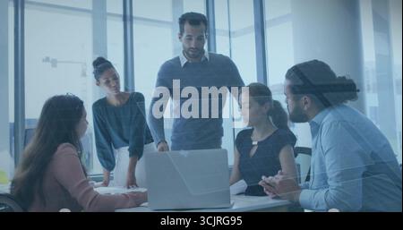 Leading Middle Eastern man wearing sweater directing team in boardroom, with laptop and documents Stock Photo