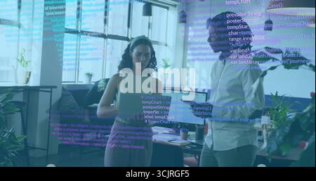 Collaborating colleagues coding on laptop and tablet in modern office, with floating code lines Stock Photo