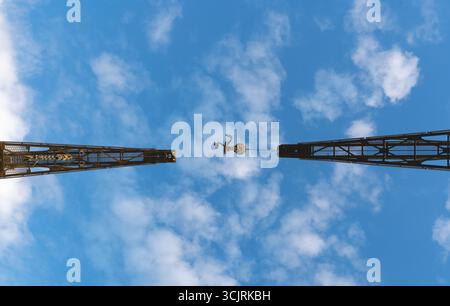 Two large industrial cranes are seen from below, framed against a clear blue sky with scattered clouds Stock Photo
