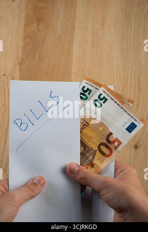 Someone is holding an envelope marked "bills" with a stack of 50 euro banknotes sticking out of the envelope Stock Photo