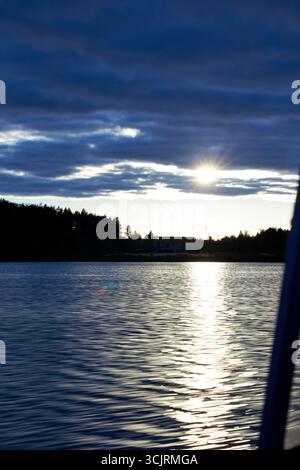 Scenic sunset over lake with dramatic cloudy sky and sun rays reflecting on water. Peaceful evening landscape with calm ripples and silhouette of tree Stock Photo