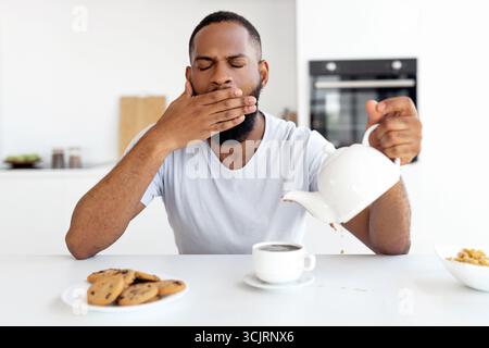 Black guy pouring coffee away from cup and yawning Stock Photo