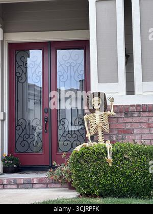 Decorative skeleton wearing a hat sits by the front entrance of a suburban home, styled for Halloween festivities Stock Photo