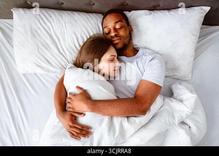 Top view of affectionate multiracial couple hugging each other while sleeping in bed Stock Photo
