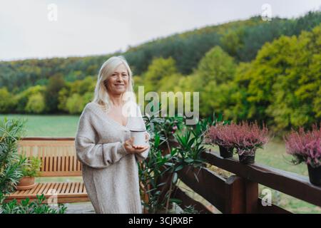 Senior woman standing terrace and drinking coffee. Stock Photo