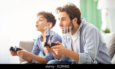 Leisure with dad. Concentrated father and son competing with each other in online video games, using joysticks Stock Photo
