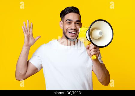 Excited arab guy speaking loud, using megaphone on yellow Stock Photo