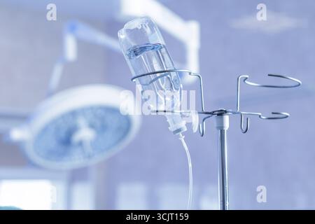 Close view of infusion bottle on a hospital stand with blurred OR light, clean sterile scene ideal for healthcare training and marketing. Stock Photo