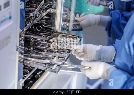 Technician in blue scrubs organizes clean metal tools on racks inside a sterilization cabinet, illustrating aseptic workflow and infection control. Stock Photo