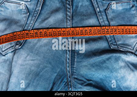 front of a pair of blue denim jeans with the button loose and a yellow and orange measuring tape on it. Stock Photo