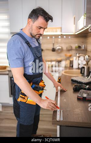 Handyman taking measurements of kitchen counter using tape measure and pencil Stock Photo