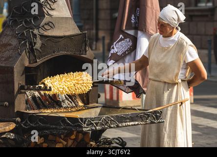 Woman preparing a tree cake, Lithuanian šakotis, Polish sękacz, Belarusian bankucha, German baumkuchen, cooked over an open fire Stock Photo