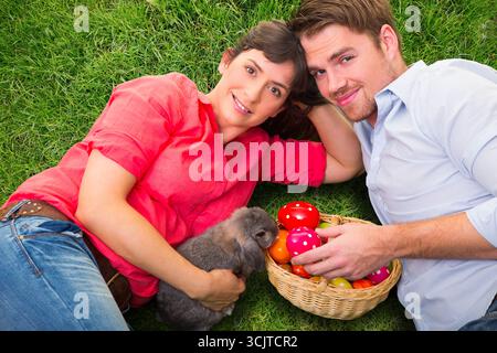 couple lying in a meadow with a rabbit and a basket full of Easter eggs Stock Photo