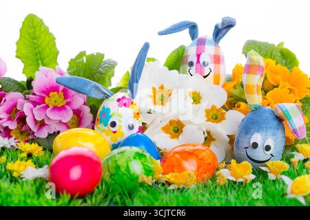 Easter eggs with bunny ears and happy faces between other Easter eggs and primroses in the grass, cut-out, composing Stock Photo