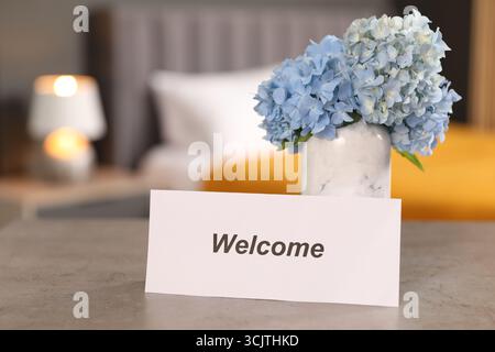 Card with word Welcome and hydrangea flowers on grey table indoors Stock Photo