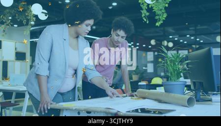 Examining designers wearing blazer and polo shirt leaning over blueprints in office, with plans Stock Photo