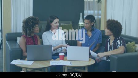 Gesturing colleagues discussing project in living room, with two laptops, documents, red coffee cup Stock Photo