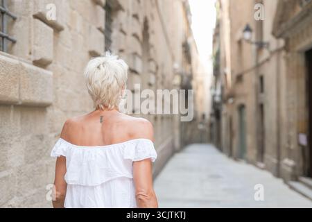 A woman in a white dress walks down a narrow street. Concept of solitude and quietness, as the woman is the only person visible in the scene. The stre Stock Photo