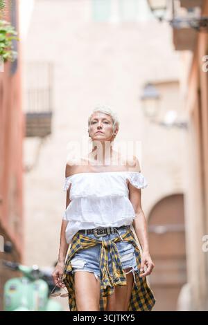 A woman wearing a white shirt and plaid shorts walks down a narrow alleyway. The scene is quiet and peaceful, with only the sound of her footsteps and Stock Photo