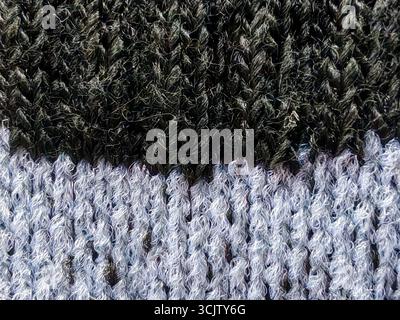 Detailed macro shot of a two-tone knitted fabric, featuring a distinct division between a dark, textured section and a lighter, fuzzy one. Stock Photo