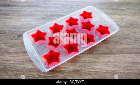 Empty red silicone star molds in a transparent tray on a wooden table Stock Photo