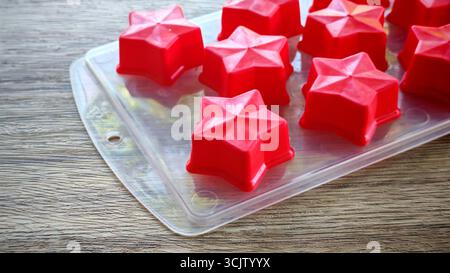 Empty red silicone star molds in a transparent tray on a wooden table Stock Photo