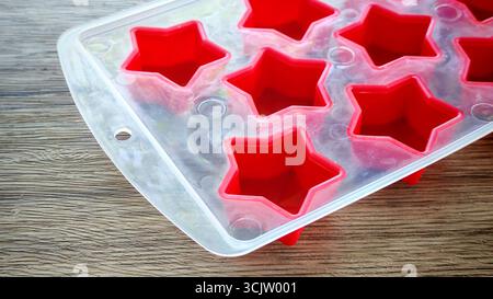 Empty red silicone star molds in a transparent tray on a wooden table Stock Photo