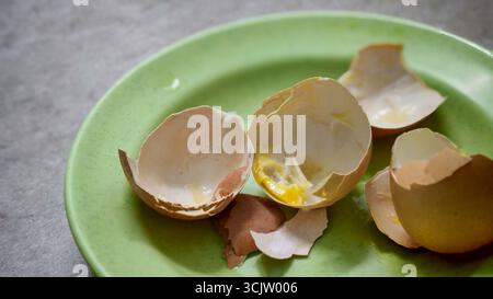 Close-up of broken egg shells on a green plate, with a hint of yolk and kitchen counter visible. Stock Photo