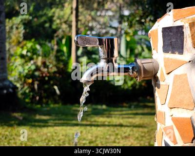A close-up of a shiny metal water faucet mounted on a wall decorated with mosaic tiles in shades of brown, cream, and black Stock Photo