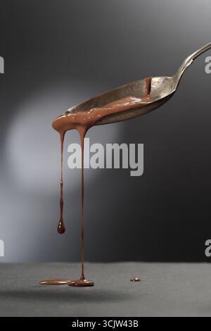 Sweet liquid chocolate flows from a tilted metal spoon against a dark background Stock Photo