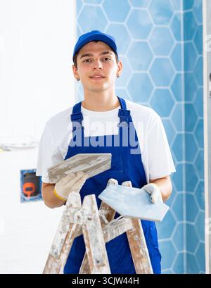 Construction worker in work clothes engaged in wall tiling work during overhauls indoors Stock Photo