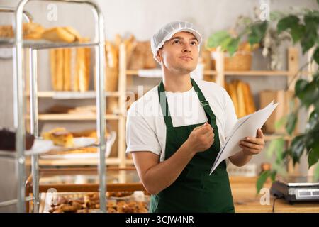 Thoughtful young baker looking over papers in craft bakery Stock Photo