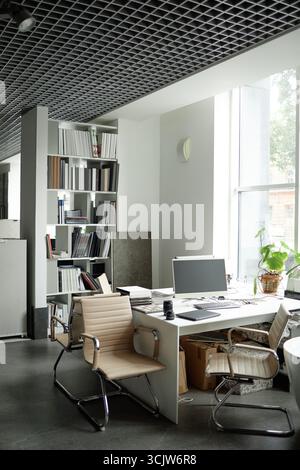 Empty Modern Office Workspace Featuring Computer and Bookshelves by Window Stock Photo