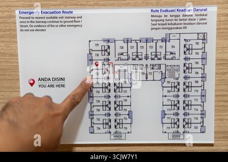 Finger indicates evacuation path on a building floor plan displayed on wooden surface Guidance for emergency situations is perfect for facility safety Stock Photo