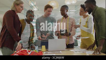 Collaborating group of designers leaning around table in design studio with laptop, measuring tape Stock Photo