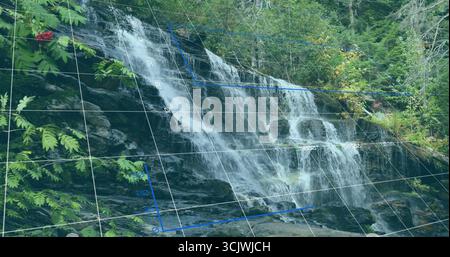 Cascading waterfall flowing over layered rocks at woodland creek, with green ferns and grid overlay Stock Photo